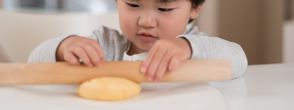 toddler baking ideas - the photo shows a child using a rolling pin to roll some dough