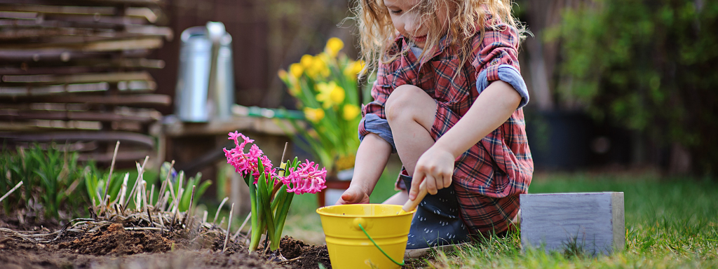 spring activities for kids -the photo shows a girl crouching down in a garden next to some flowers with a bucket