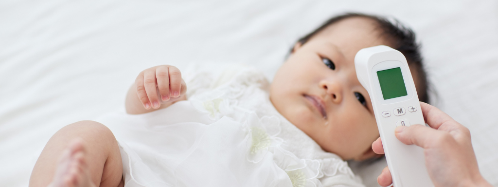 baby shower gifts - the photograph shows a baby with someone holding a baby thermometer above their forehead